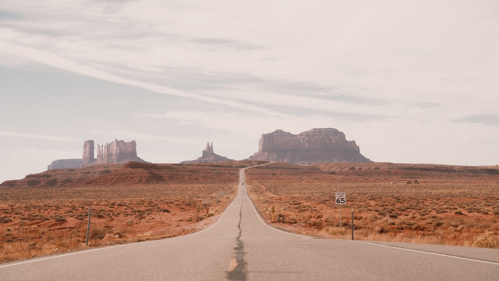 Straight highway stretching toward Monument Valley buttes under cloudy sky
