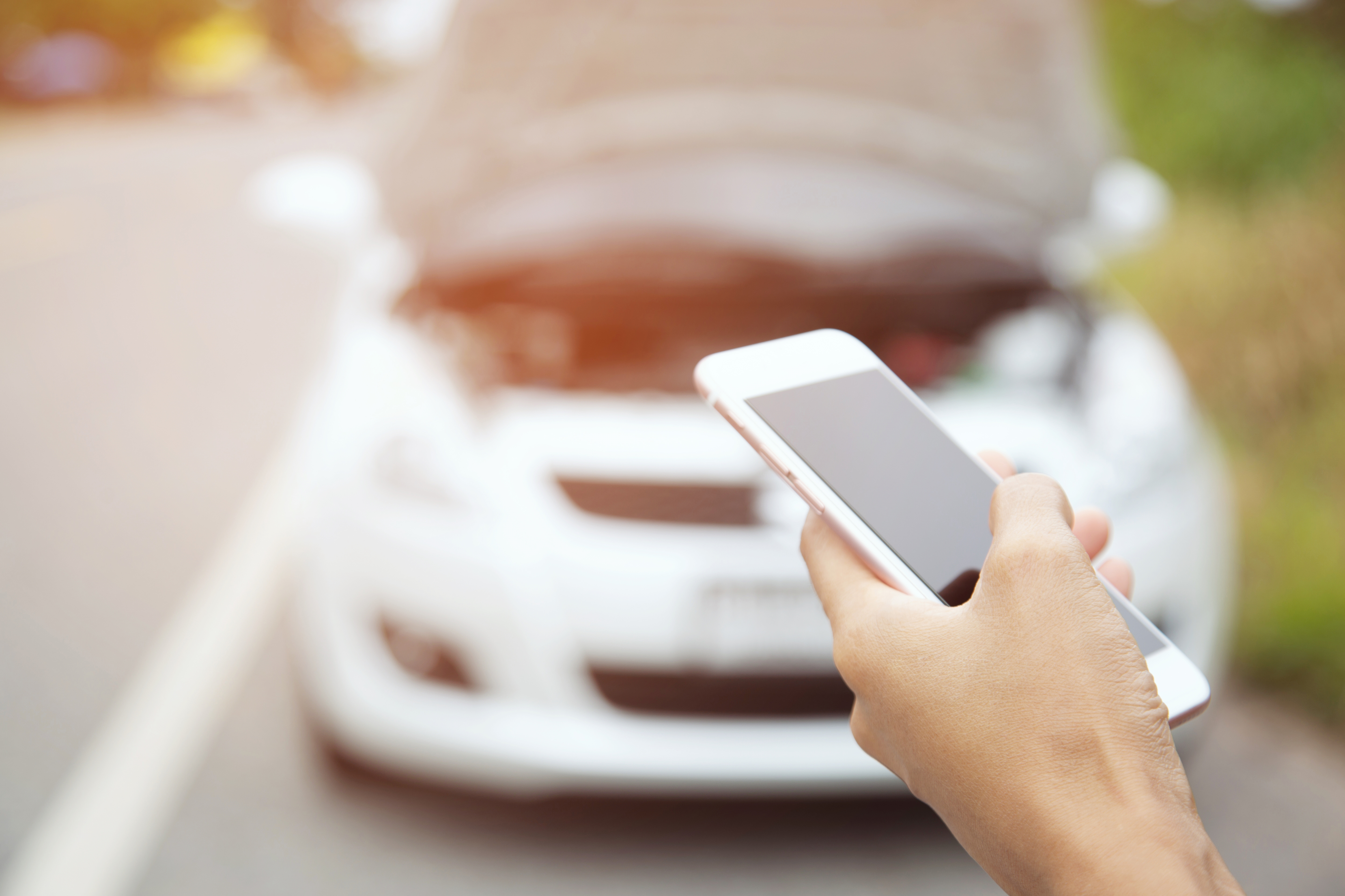 Person holding smartphone with blurred car in background