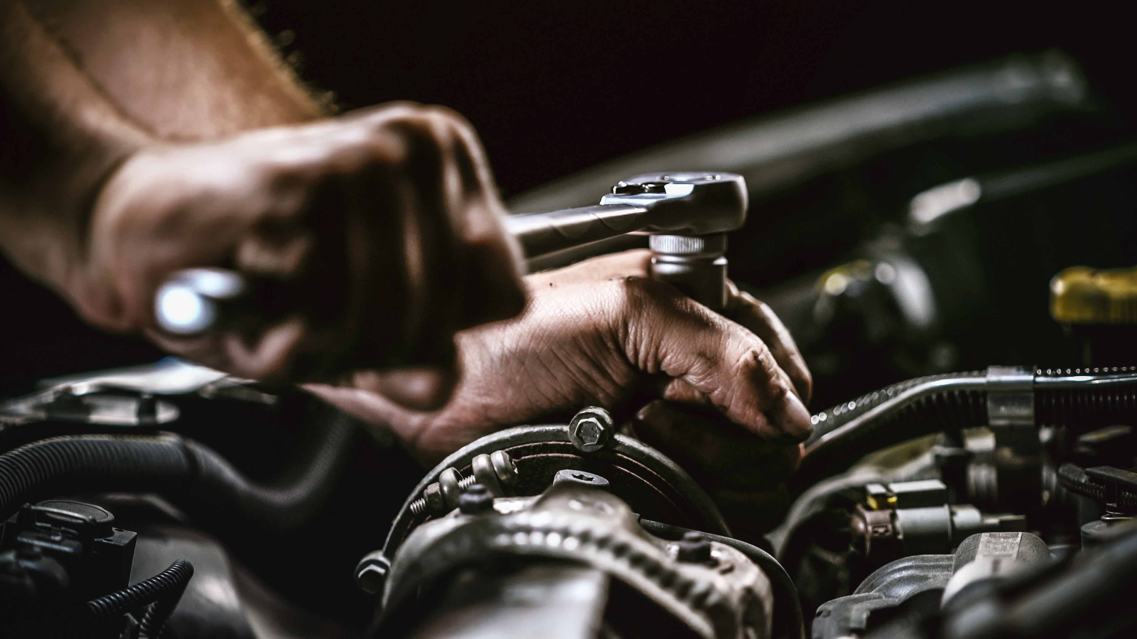 Mechanic's hands adjusting engine components with wrench during vehicle maintenance