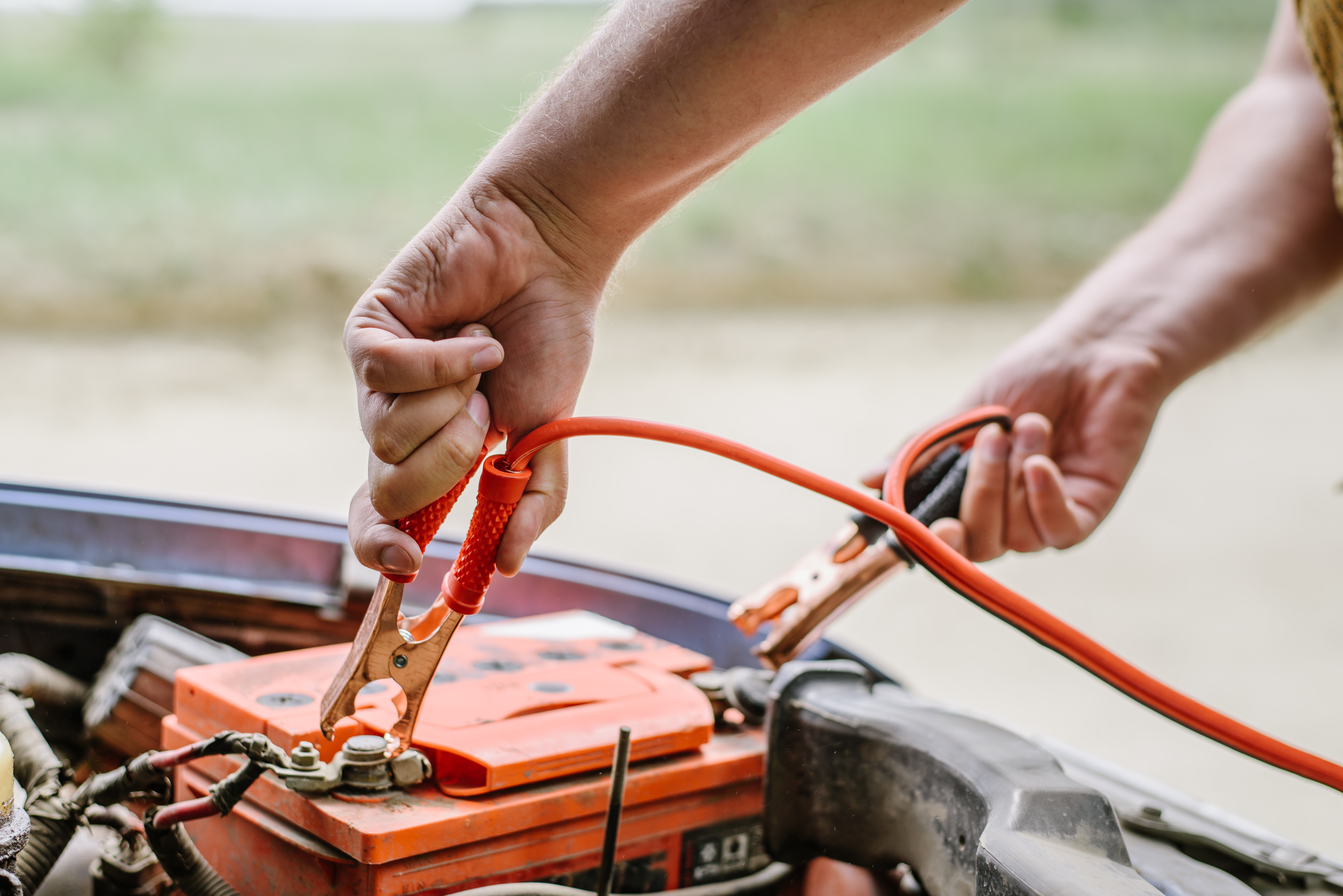 Two people connecting jumper cables to a car battery during roadside assistance